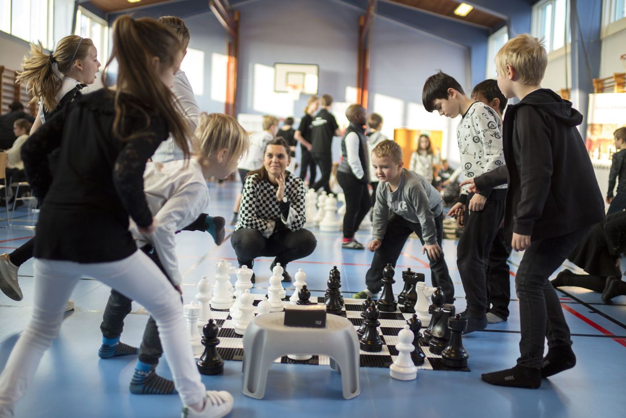 otte elever på mellemtrinnet står om et skakbræt på gulvet