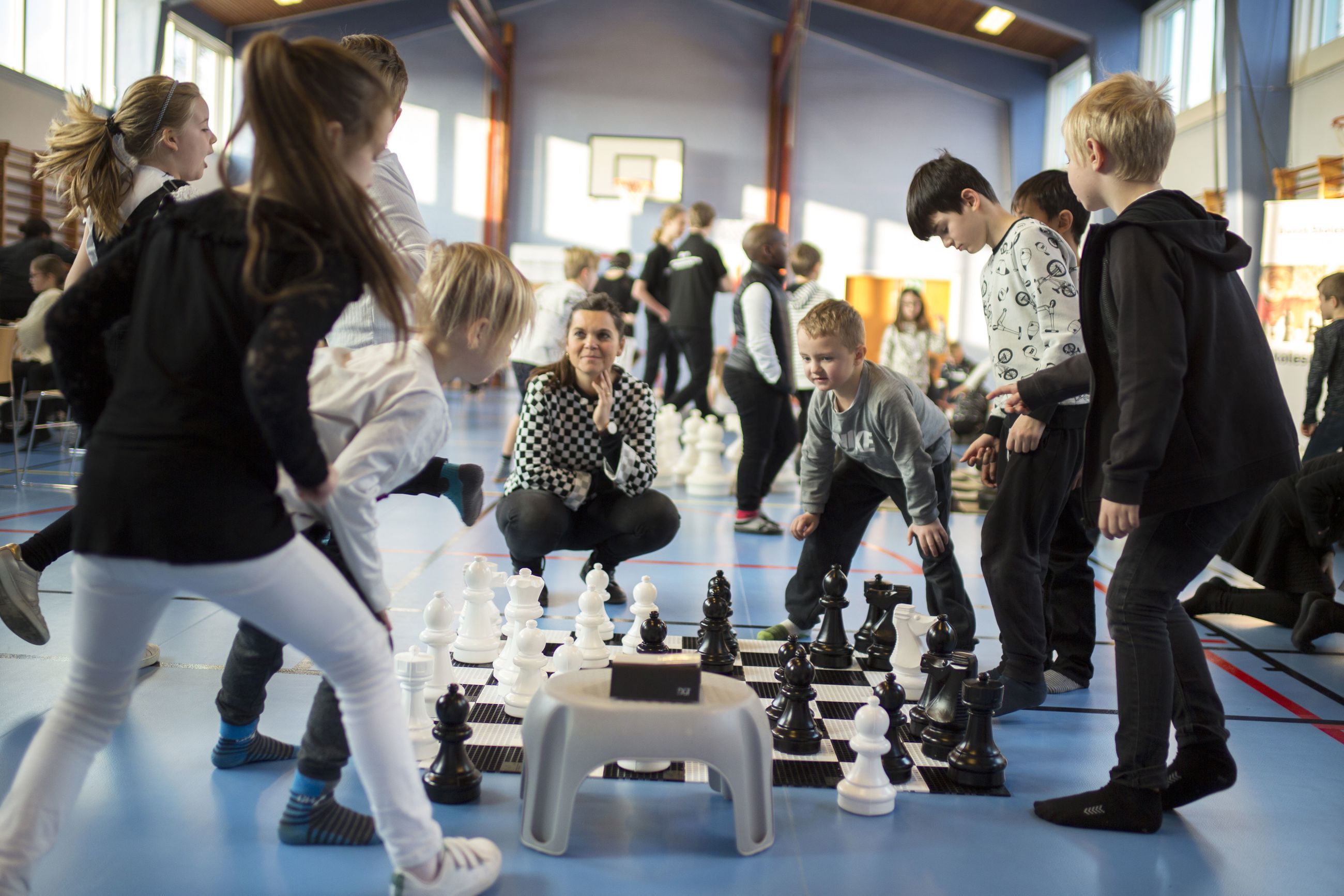 otte elever på mellemtrinnet står om et skakbræt på gulvet